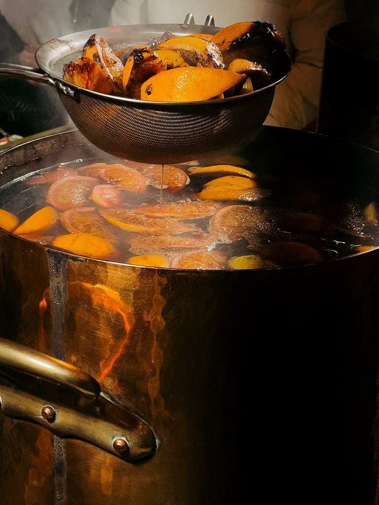 Close-up of brewing mulled wine with oranges and spices in a pot, exuding warmth and festivity.