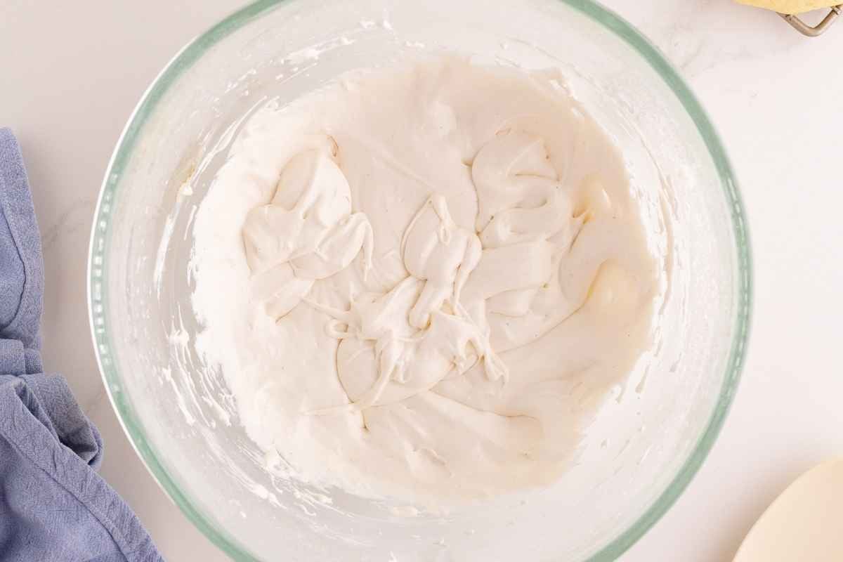Fluffy white marshmallow cream swirled into a glass mixing bowl beside a blue linen napkin.