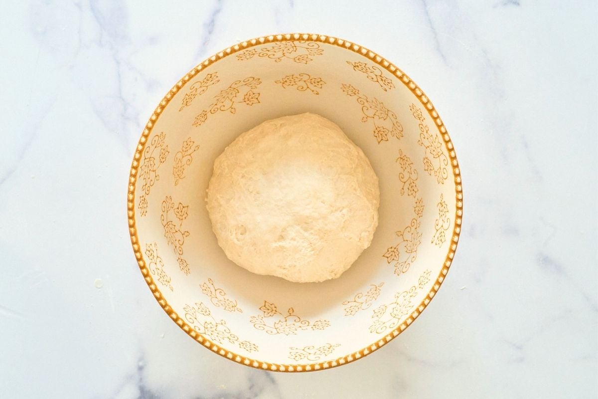 Smooth ball of sourdough resting for its first rise in a gold-patterned ceramic bowl.