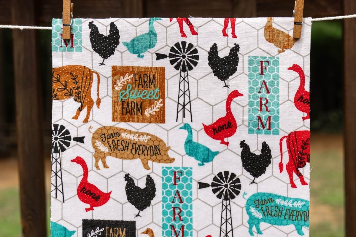 Farmhouse-print fabric with chickens, pigs, and windmills clipped to a clothesline to air dry.