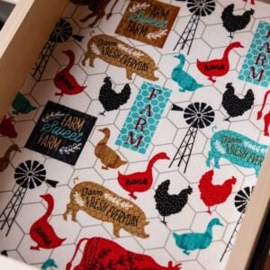 Farmhouse-print fabric drawer liner featuring pigs, chickens, ducks, windmills, and Farm Sweet Farm text inside a wooden drawer.