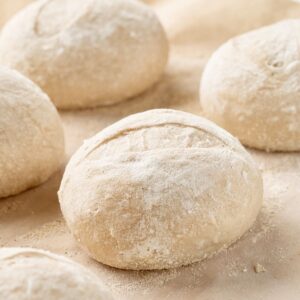Round balls of floured French roll dough resting on parchment paper before baking.