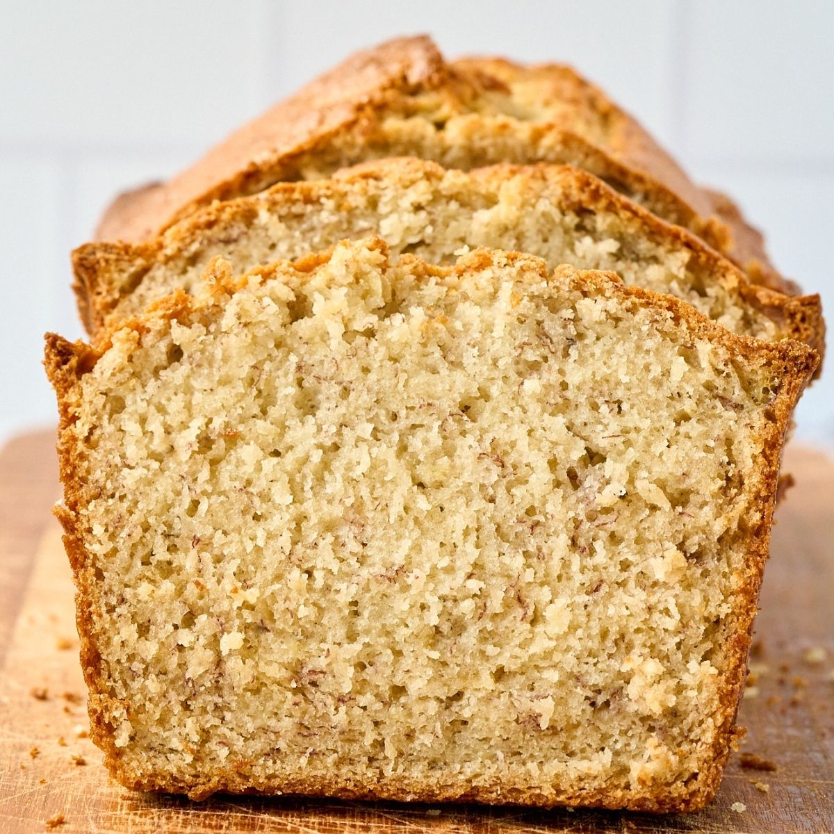 Sliced loaf of golden banana bread showing moist crumb and crisp crust on a wooden cutting board.