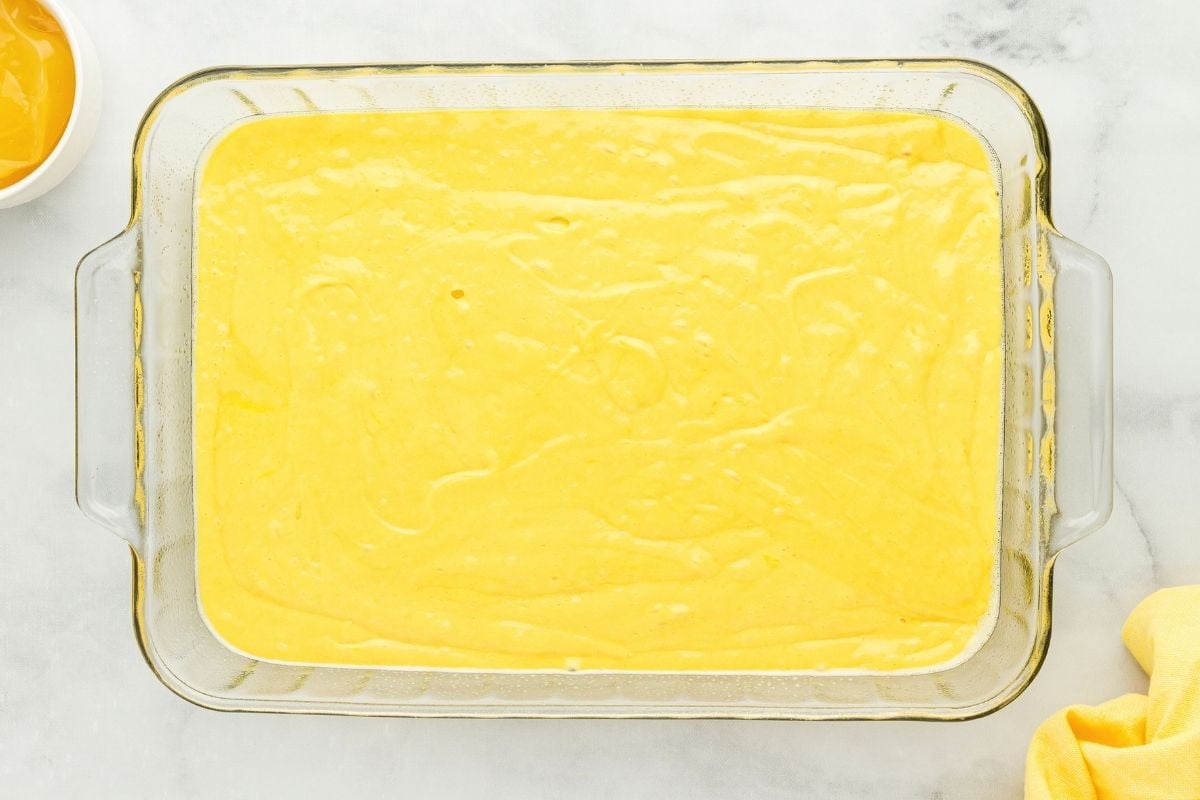 Smooth yellow lemon cake batter spread evenly in a glass baking dish on marble.