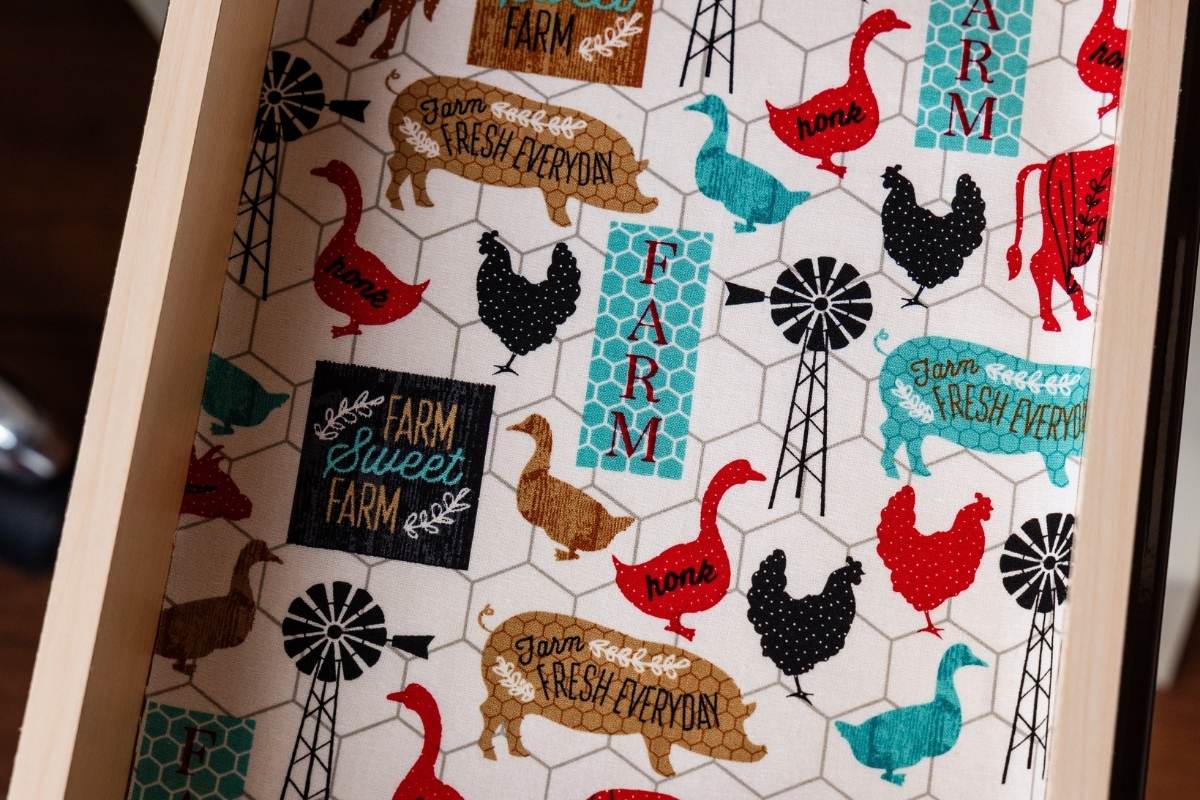 Farmhouse-print fabric liner featuring pigs, chickens, ducks, and windmills laid inside a wooden drawer.