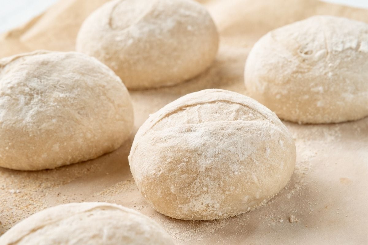 Round balls of flour-dusted French roll dough resting on parchment paper before baking.