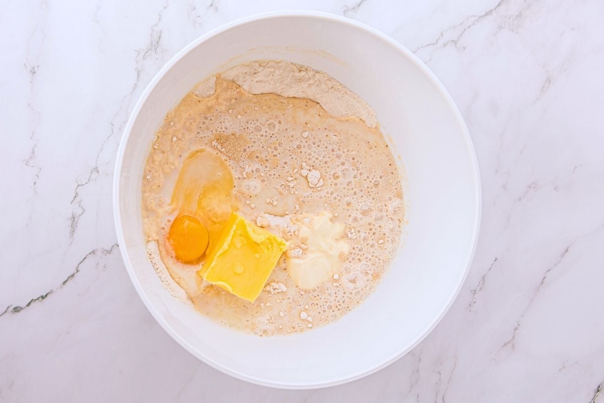 Egg, butter, and sour cream added to bubbly yeast mixture in a white mixing bowl.
