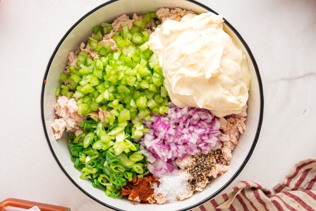 Shredded chicken, diced celery, red onion, green onion, mayonnaise, paprika, salt, and pepper combined in a white bowl.