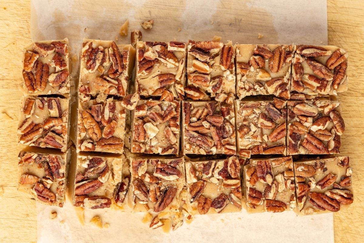 Squares of pecan-topped penuche fudge cut into even pieces on parchment over a wooden board.
