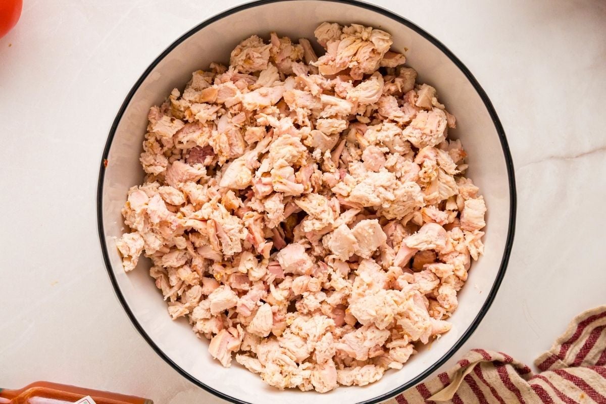 Diced smoked chicken cooling in a large white bowl with black rim on a marble surface.