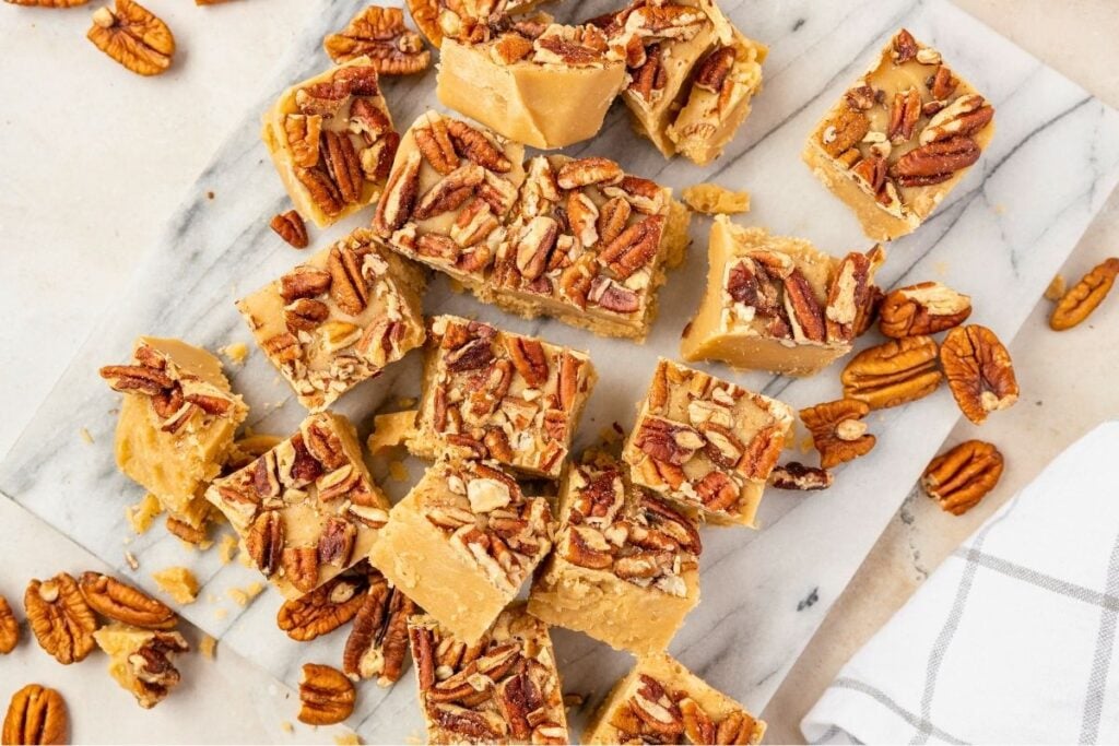 caramel-colored, pecan topped fudge squares cut up on a marble cutting board