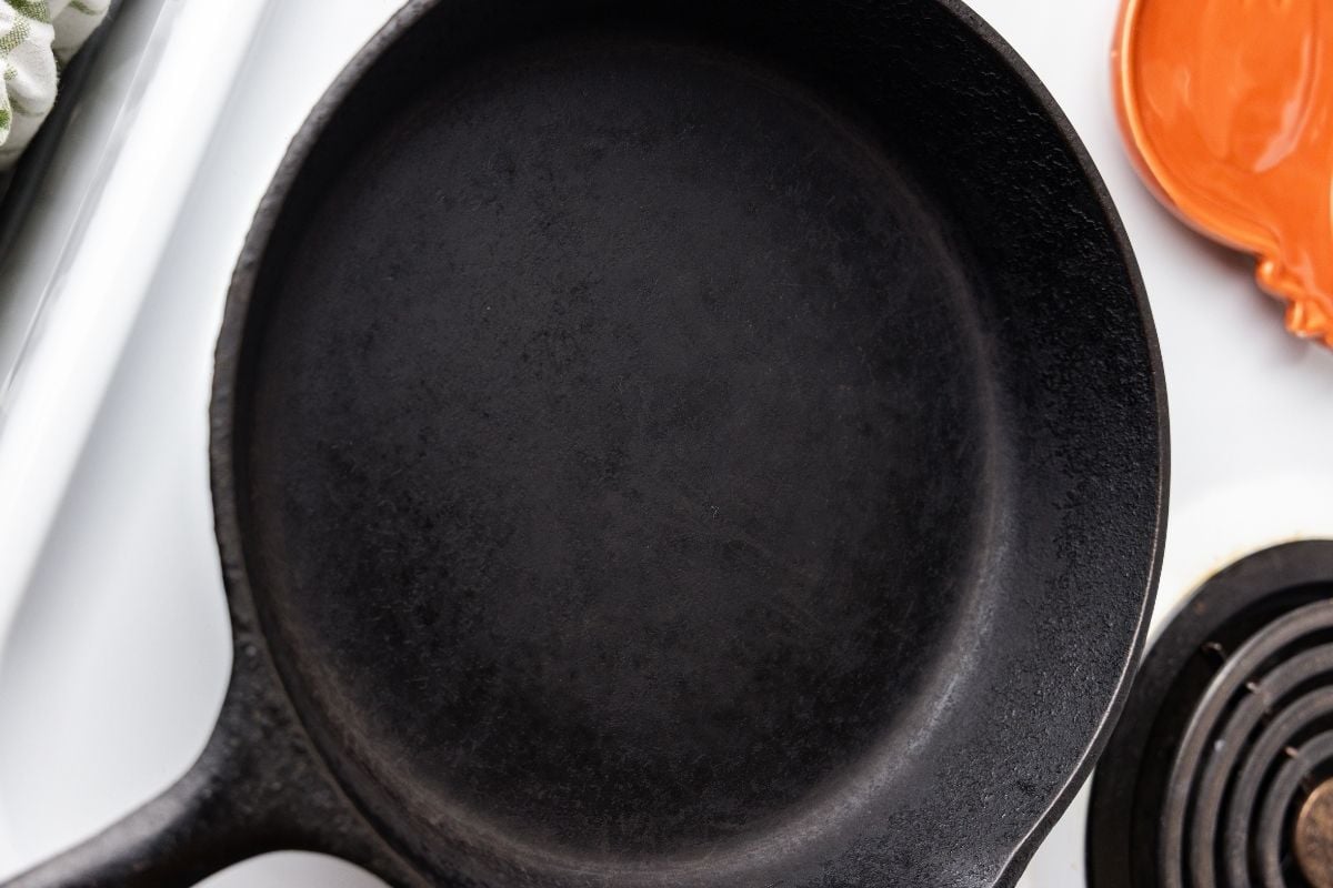 Empty clean black cast iron skillet viewed from above beside an orange spatula and stove burner.