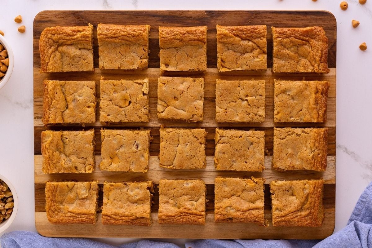 Twenty golden butterscotch bars cut into squares on a wooden cutting board with scattered butterscotch chips nearby.
