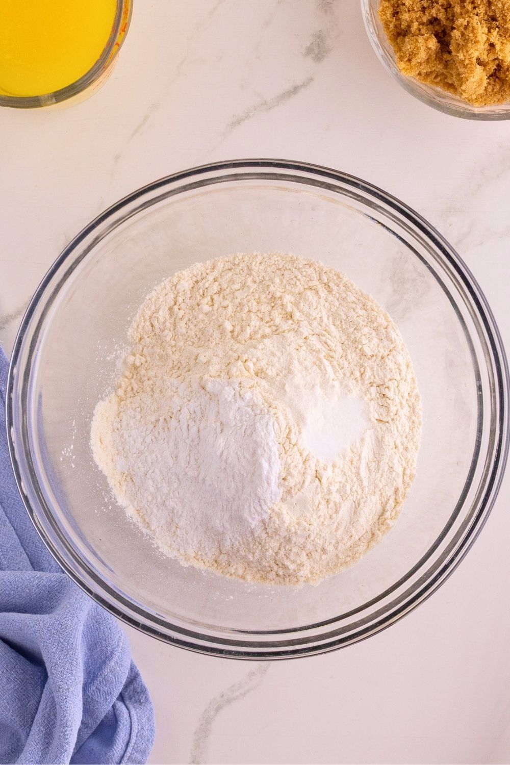 Flour and leavening agents combined in a glass bowl beside melted butter and brown sugar.