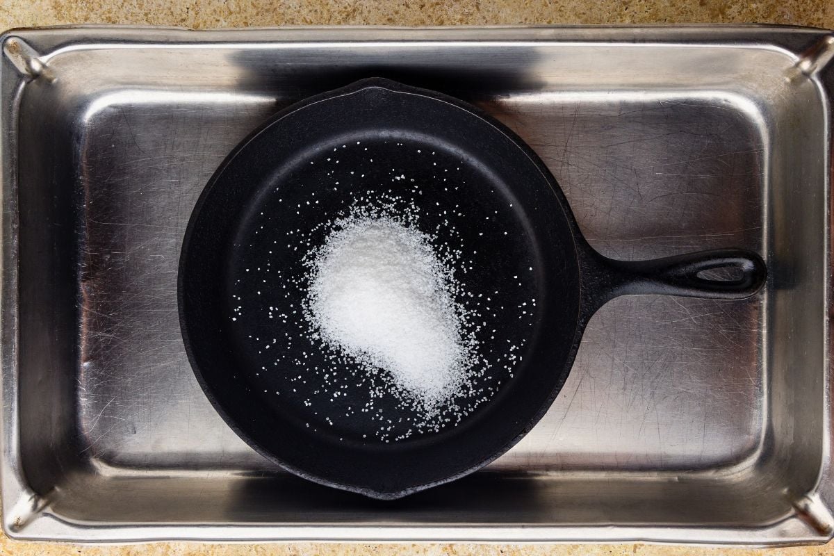 Coarse salt poured into a black cast iron skillet resting in a stainless steel sink.