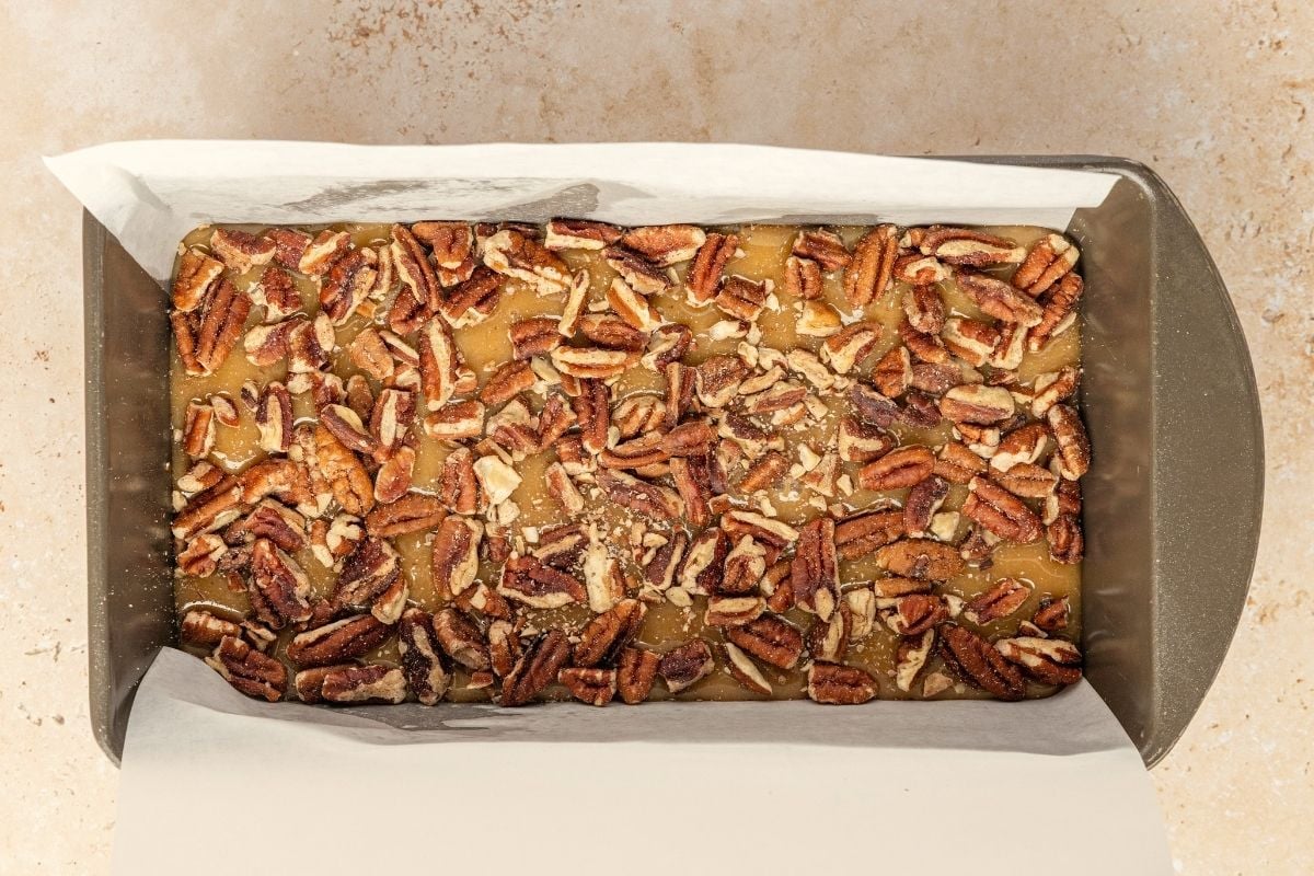 Caramel-colored penuche fudge spread into a parchment-lined loaf pan and topped with chopped pecans.