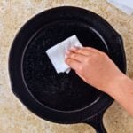 someone wiping the inside of a cast iron skillet with a towel and oil