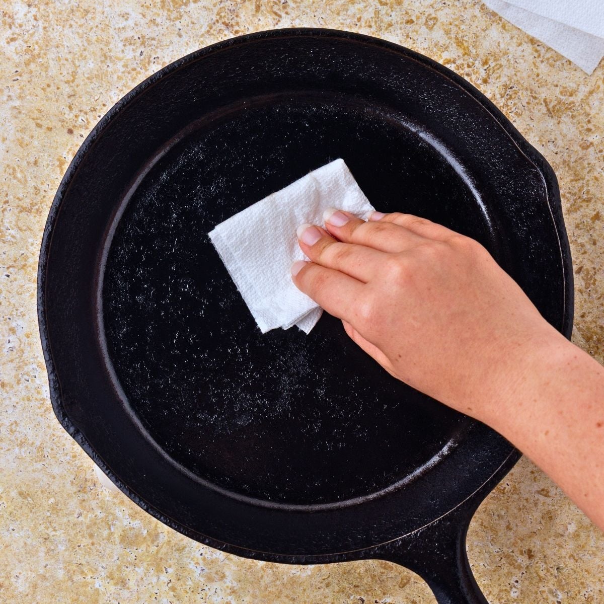 someone wiping the inside of a cast iron skillet with a towel and oil