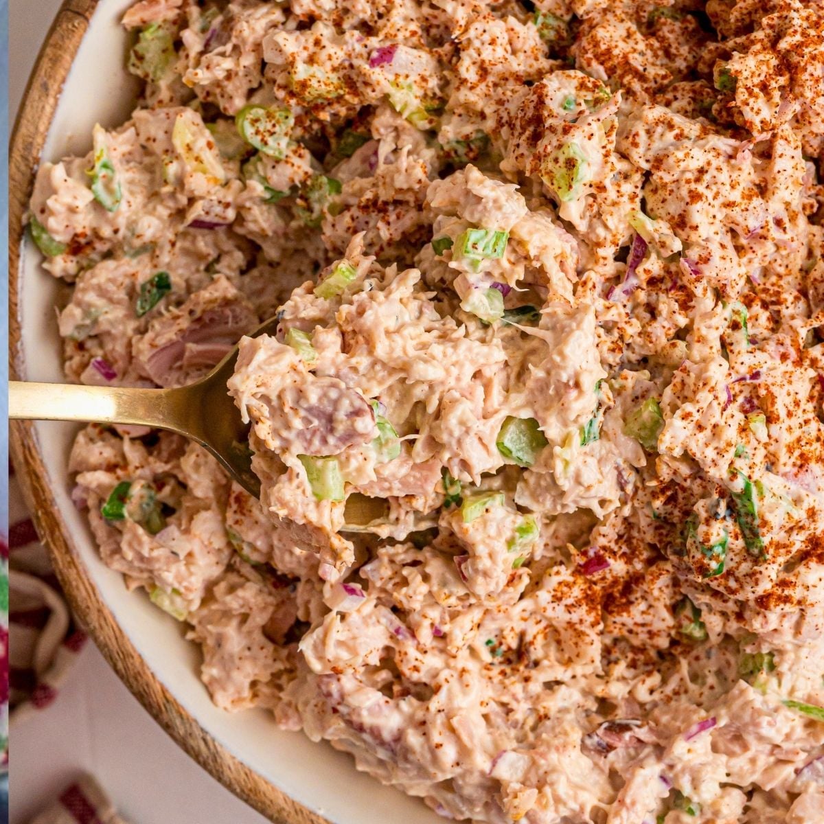Gold spoon lifting creamy smoked chicken salad with celery, red onion, and paprika from a bowl.