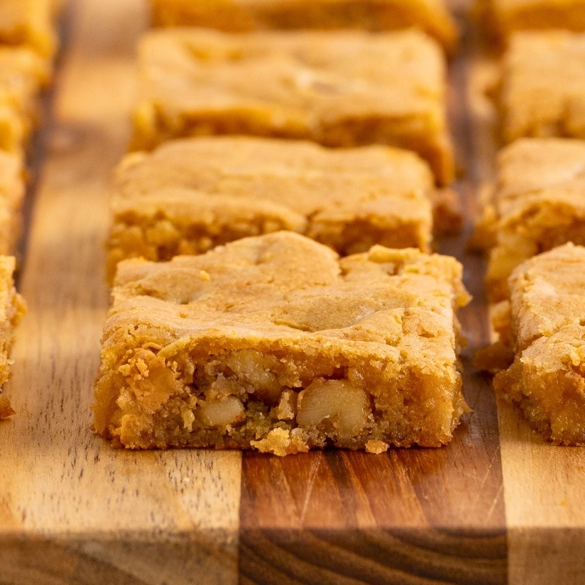Golden butterscotch bars cut into squares and arranged in rows on a wooden cutting board.