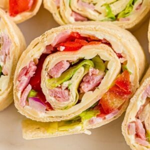Close-up of tortilla pinwheels filled with ham, lettuce, red peppers, onion, and cream cheese on a light surface.