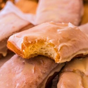 Stack of glazed maple bar donuts with a bite taken from the top one revealing fluffy interior.