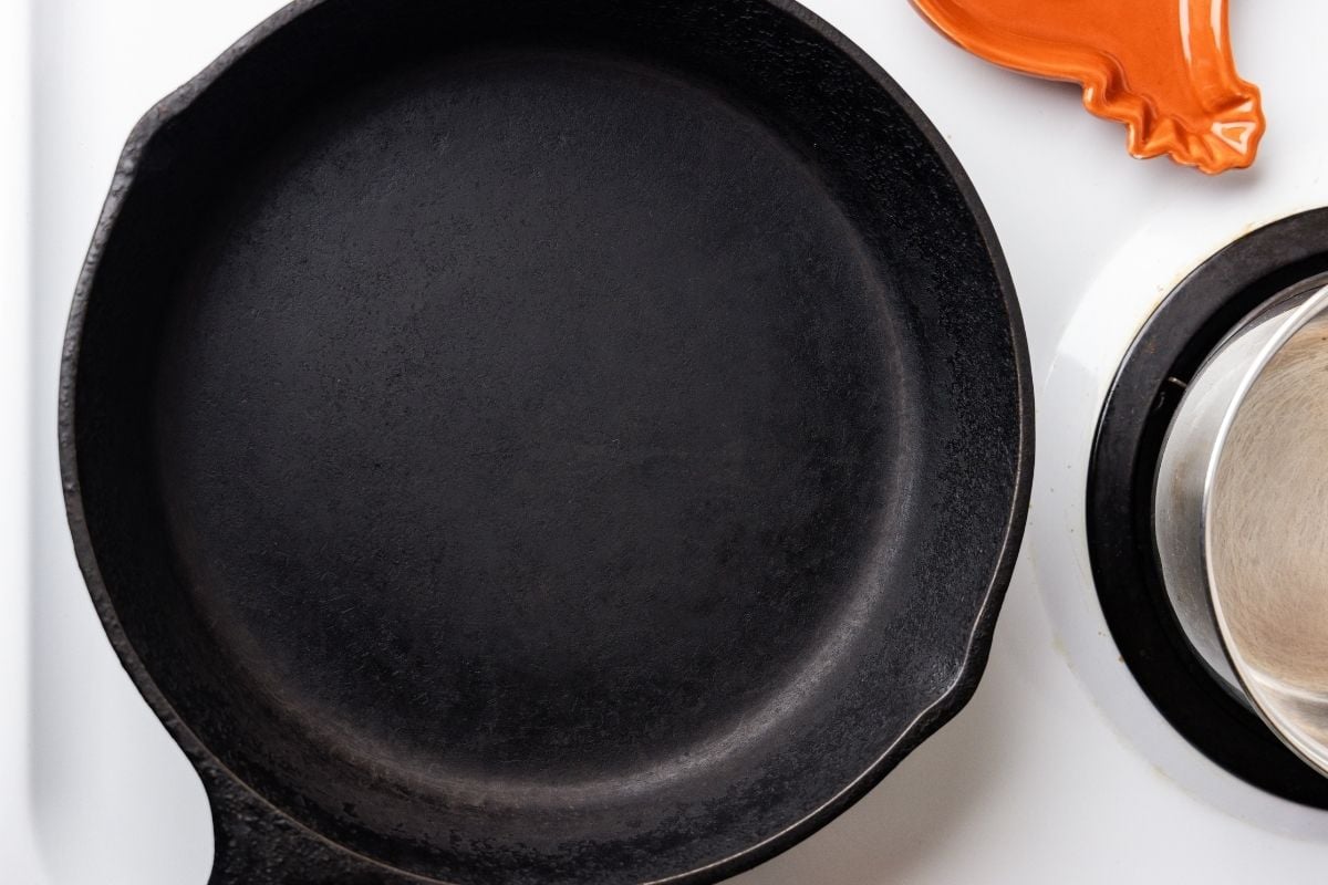Empty seasoned cast iron skillet on a white stovetop next to an orange spoon rest.