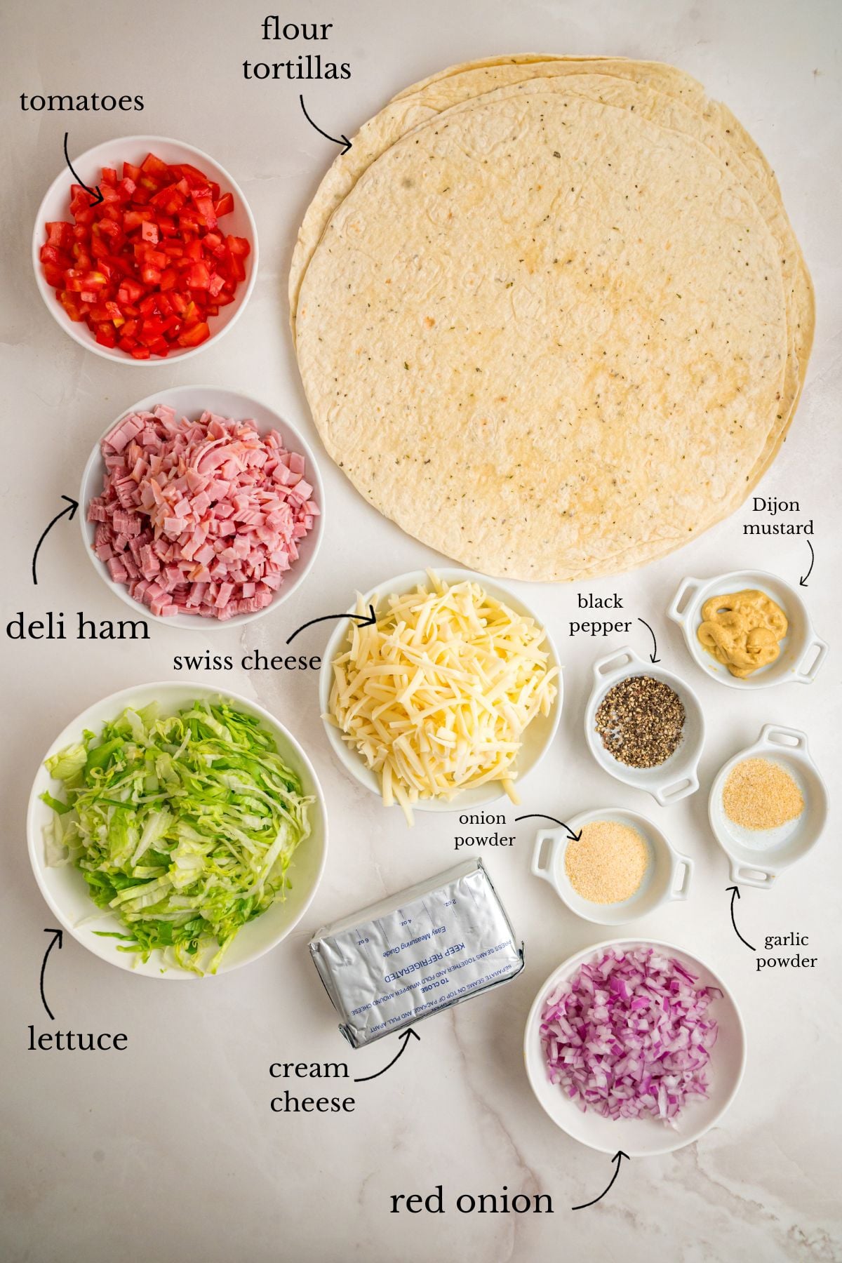 Labeled bowls of diced tomatoes, ham, shredded swiss, lettuce, red onion, spices, cream cheese, and flour tortillas.