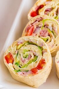 Sliced tortilla pinwheels filled with ham, lettuce, red pepper, and onion arranged on a white platter.