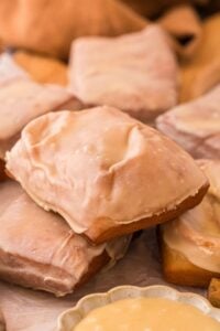 Stack of rectangular maple bar donuts coated in glossy maple glaze on parchment with a small bowl of icing.
