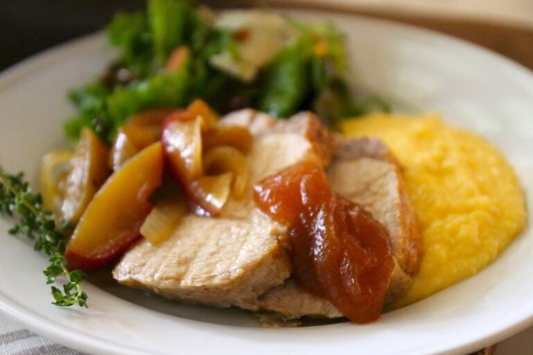 sliced pork with apples on top and a side of vegetables and polenta