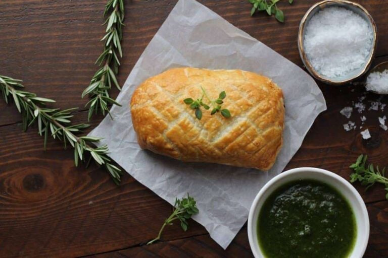 whole beef wellington on a napkin with herbs and a sauce on the side