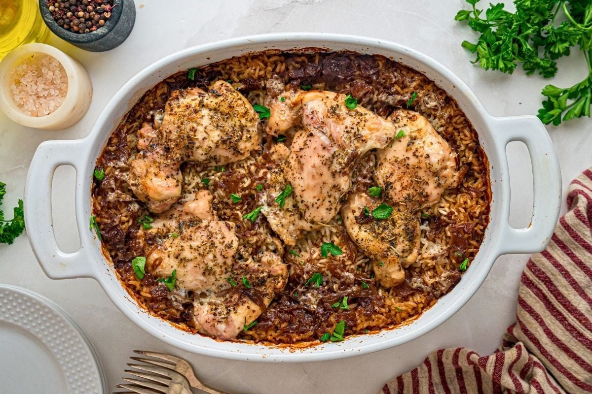 Baked chicken thighs resting on caramelized onion rice in a white oval dish, garnished with fresh parsley.