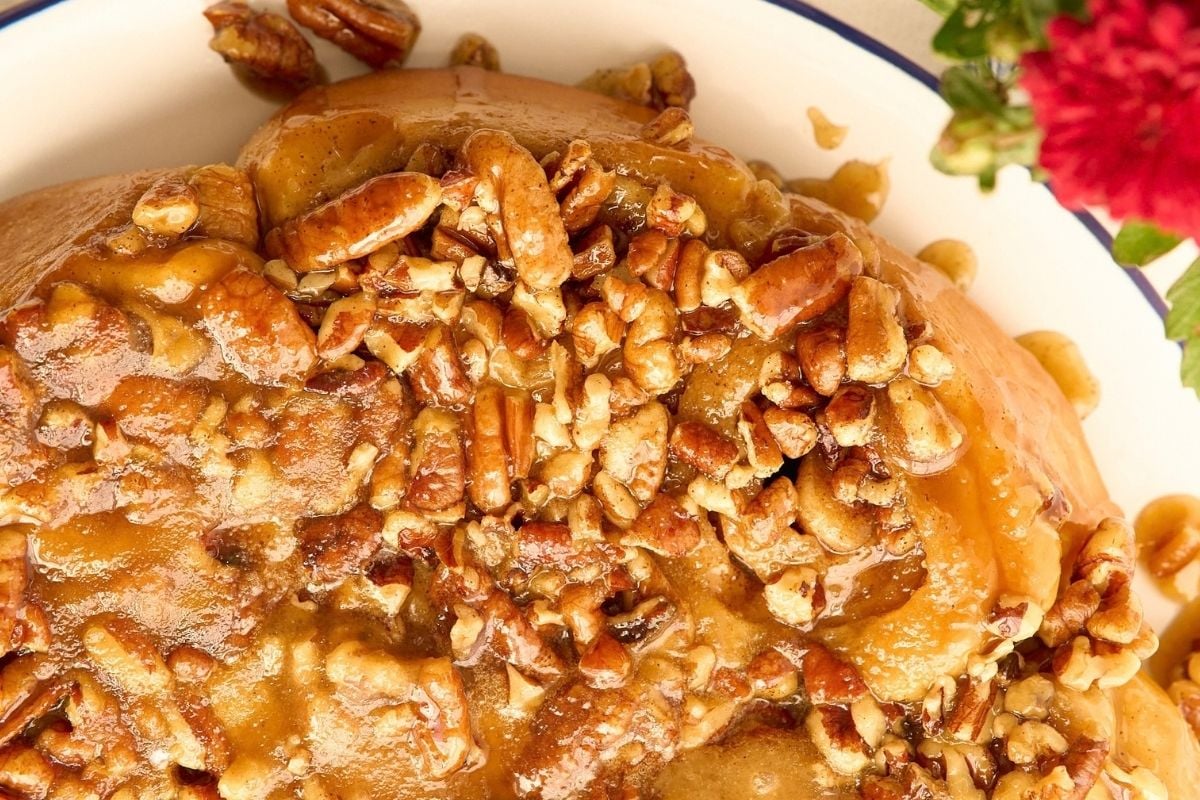 Gooey sourdough sticky buns topped with caramel glaze and chopped pecans in a blue-rimmed white dish.