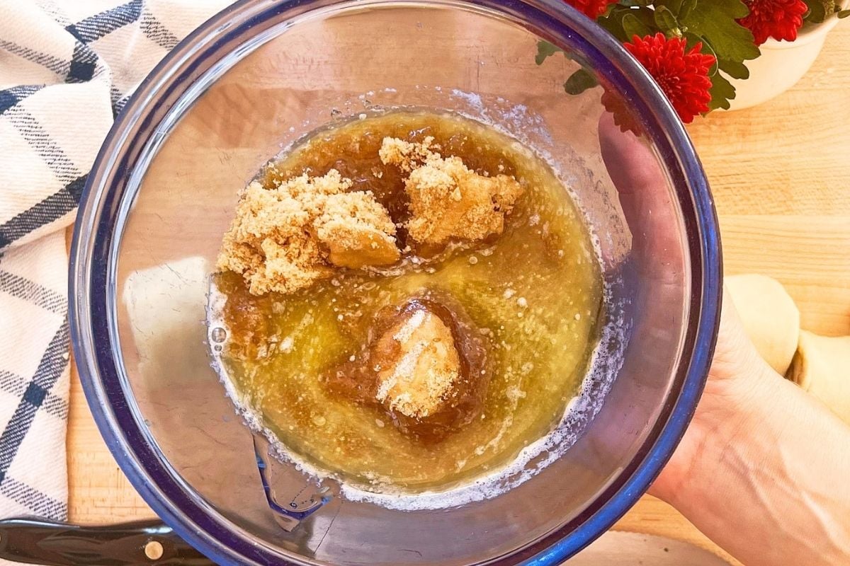 Brown sugar being added to melted butter in a glass bowl to make sticky bun topping.