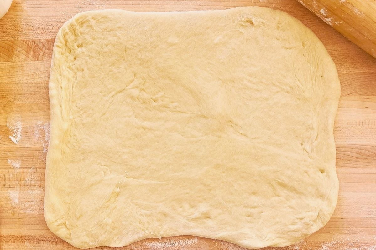 Rectangle of sourdough rolled out on a floured wooden board beside a rolling pin.