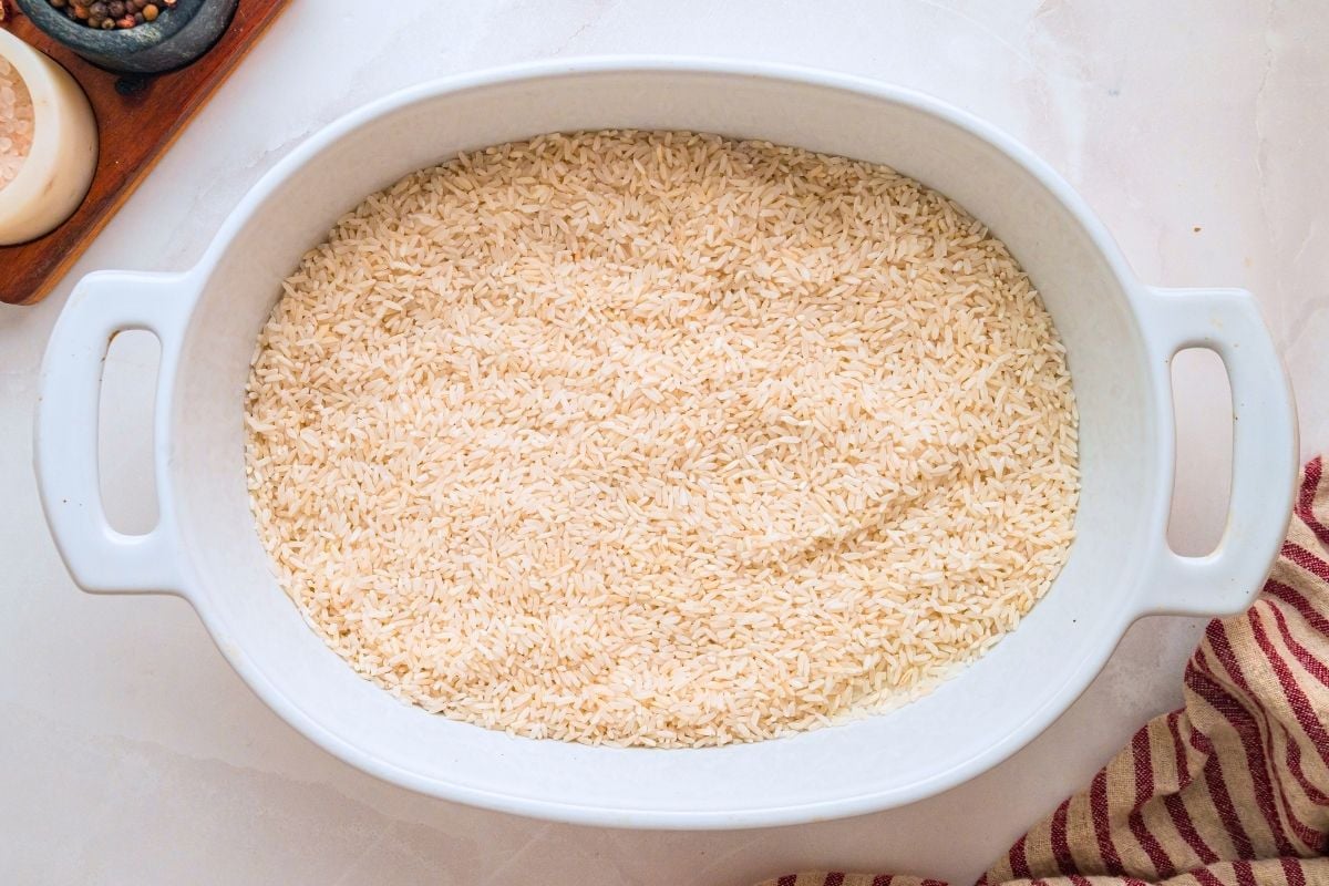Uncooked white rice spread evenly across the bottom of a white oval baking dish.