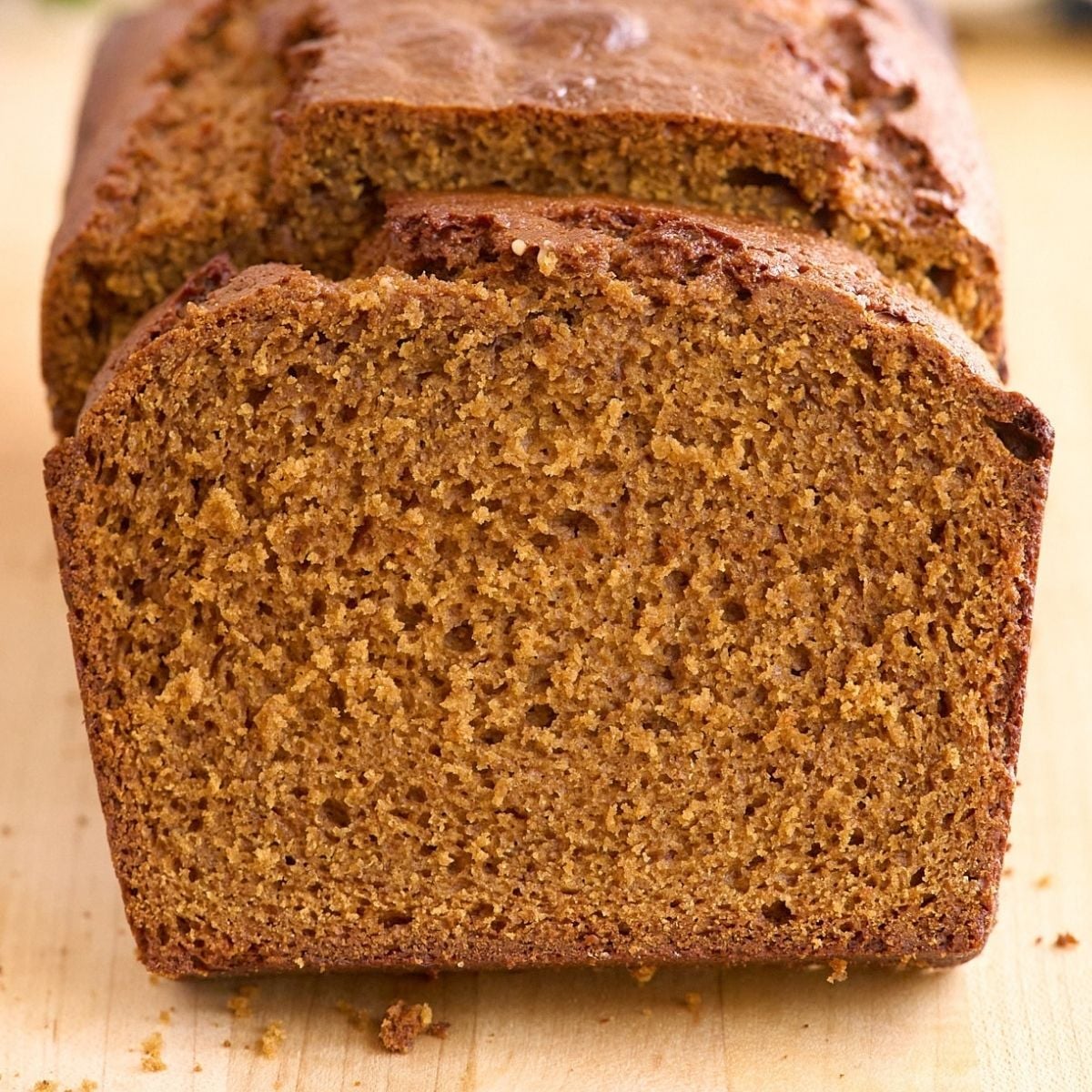 Sliced loaf of dark brown gingerbread showing moist crumb texture on a wooden cutting board.