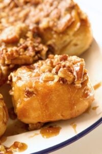 Gooey pecan-topped sticky buns glazed with caramel sauce on a blue-rimmed white enamel plate.