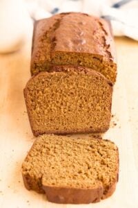 Sliced loaf of golden-brown sourdough gingerbread on a light wood board with checkered towel behind.