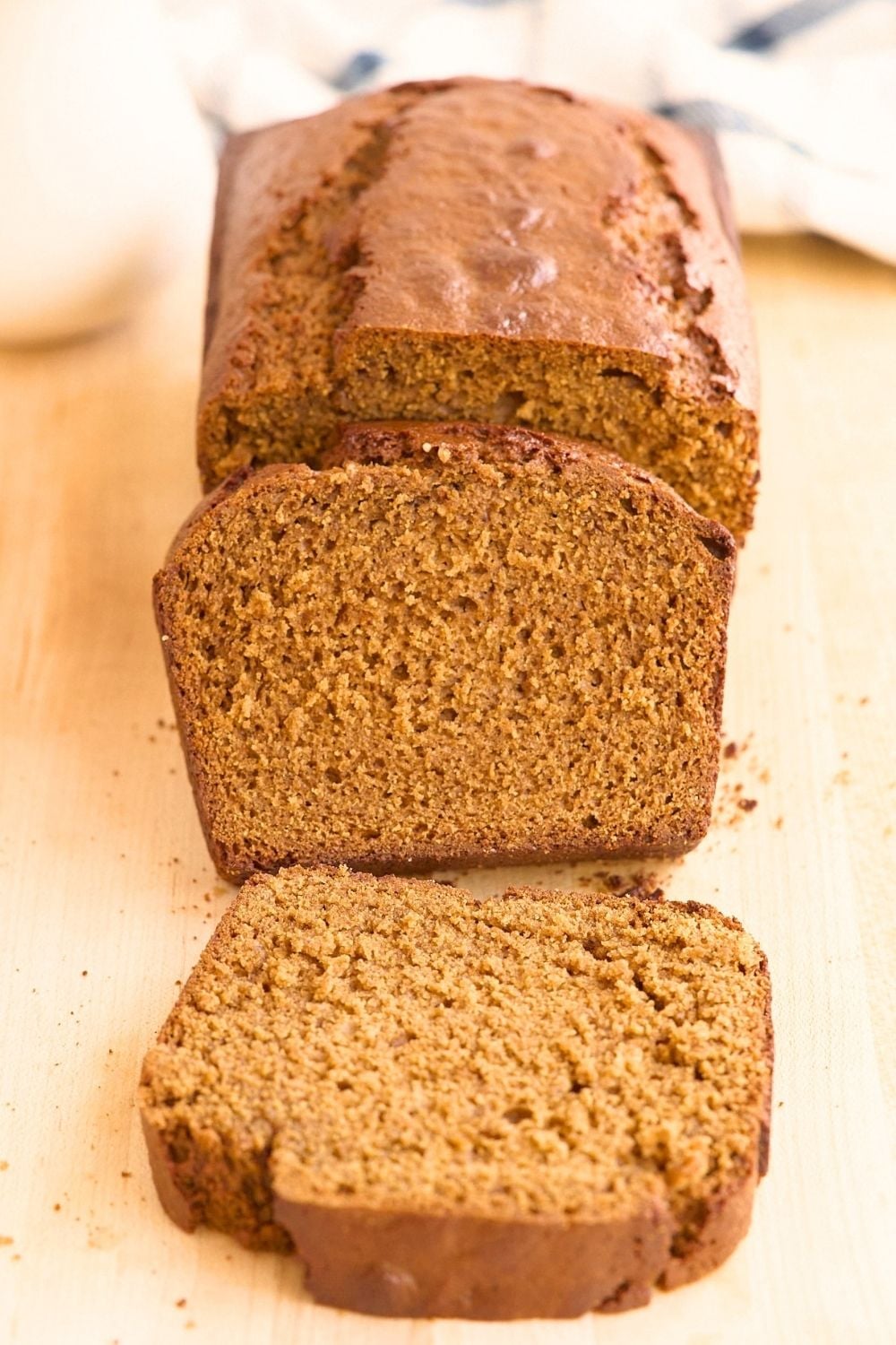 Sliced loaf of golden-brown sourdough gingerbread on a light wood board with checkered towel behind.