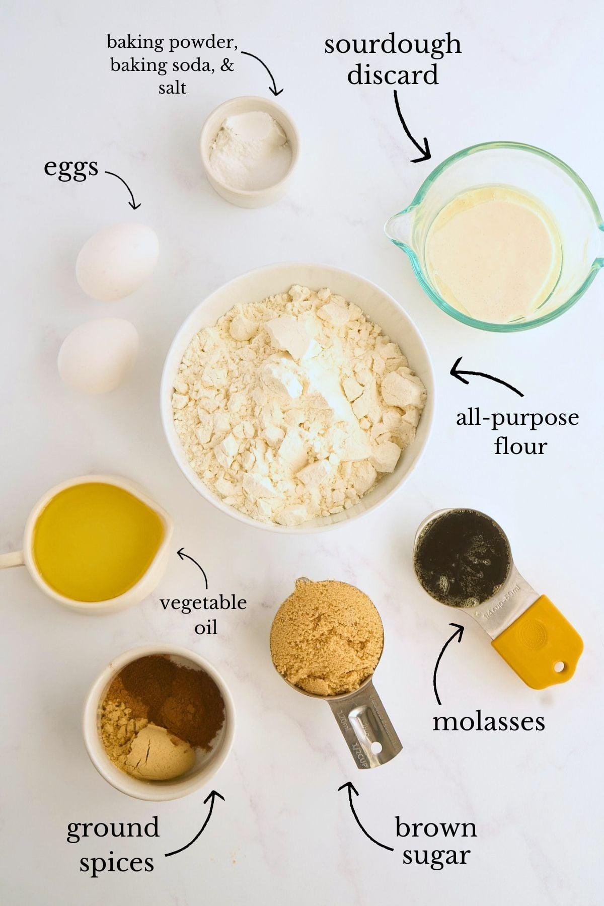 Labeled ingredients for sourdough discard gingerbread including flour, eggs, molasses, brown sugar, oil, spices, and leavening on marble.